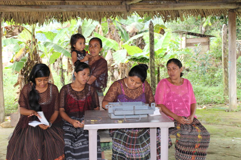 Women's savings group in Ixcan, Guatemala, sit together and look at their savings box and ledger.