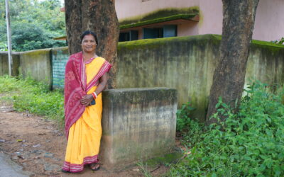 Trickle Up participant, Nepur Majhi, poses with the wall she built for school children in her village as an elected local representative in Desil, Balangir, Odisha.