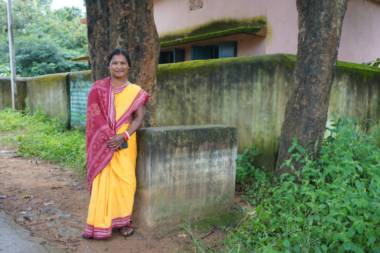 Trickle Up participant, Nepur Majhi, poses with the wall she built for school children in her village as an elected local representative in Desil, Balangir, Odisha.